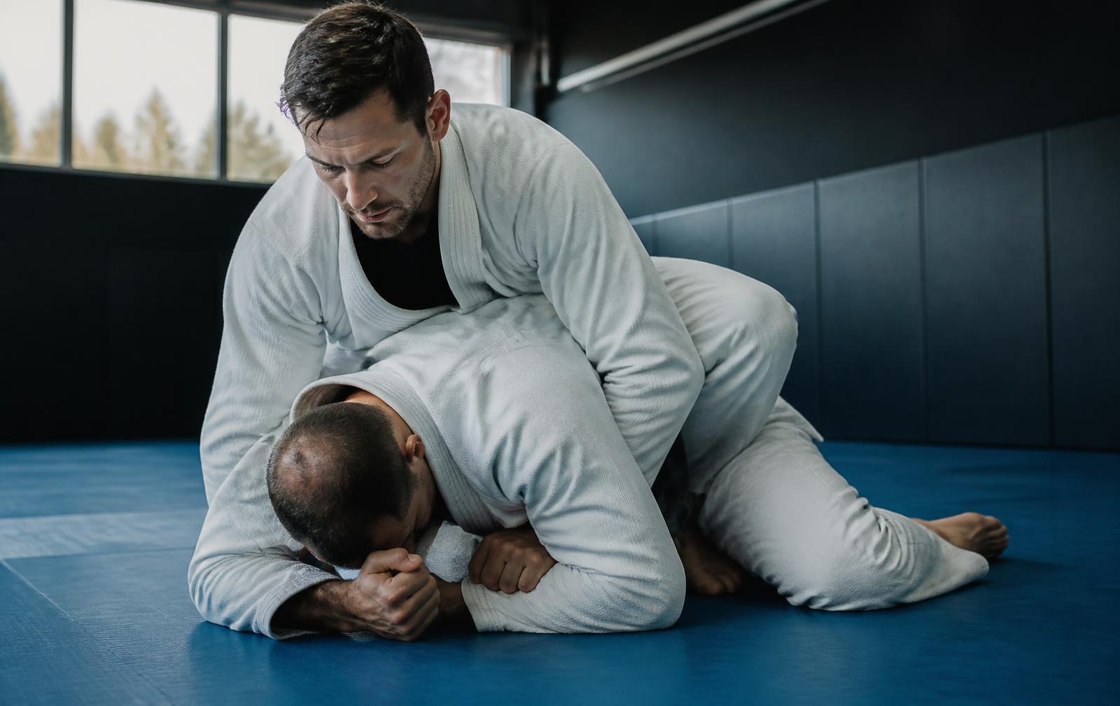 Two adults training Brazilian Jiu-Jitsu on blue mats at Cross Collar Jiu Jitsu